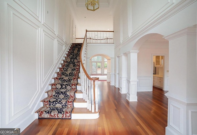 foyer with french doors, a towering ceiling, decorative columns, ornamental molding, and dark wood-type flooring