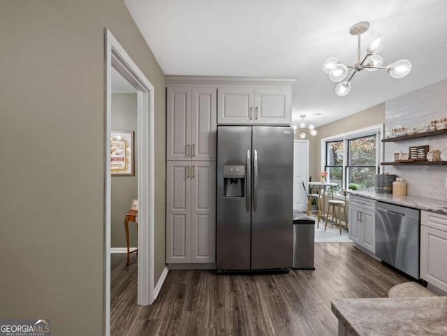 kitchen featuring light stone countertops, stainless steel appliances, dark wood-type flooring, a chandelier, and hanging light fixtures