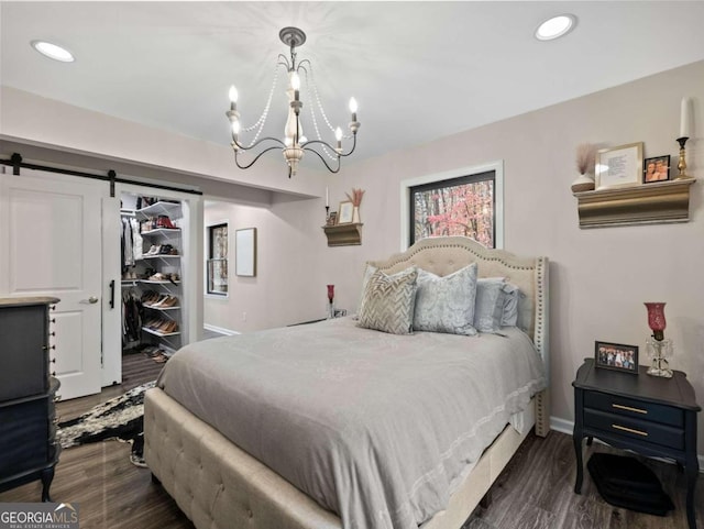 bedroom featuring a barn door, a walk in closet, dark hardwood / wood-style floors, and a notable chandelier