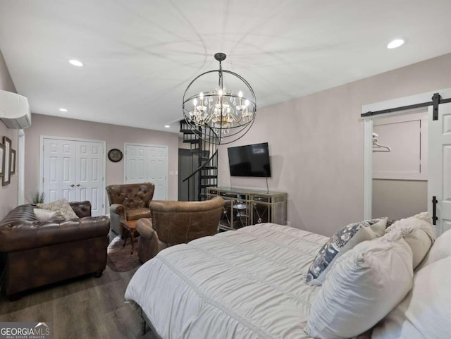 bedroom with dark hardwood / wood-style floors, a barn door, a notable chandelier, a wall unit AC, and multiple closets