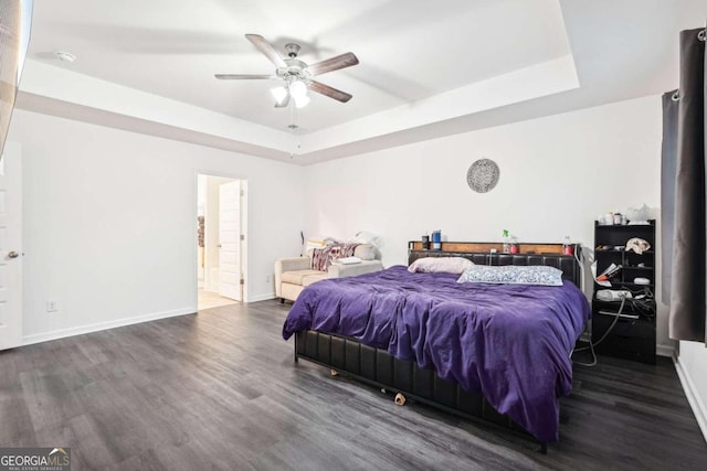 bedroom featuring a raised ceiling, ceiling fan, ensuite bathroom, and dark hardwood / wood-style floors