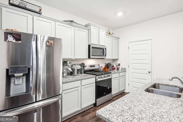 kitchen featuring light stone countertops, appliances with stainless steel finishes, dark wood-type flooring, sink, and white cabinets