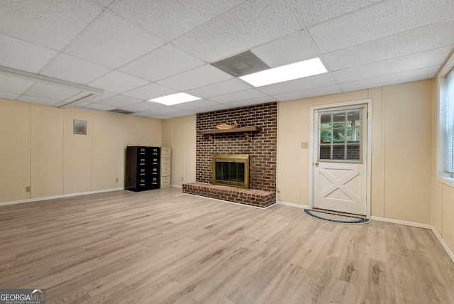 unfurnished living room featuring a drop ceiling, light hardwood / wood-style floors, and a brick fireplace