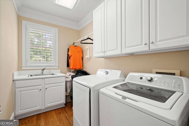 clothes washing area featuring sink, washing machine and clothes dryer, cabinets, light hardwood / wood-style floors, and crown molding