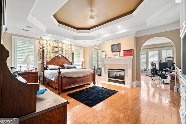 bedroom with crown molding, light hardwood / wood-style flooring, multiple windows, and a tray ceiling