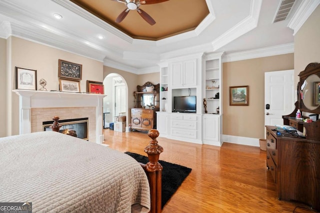 bedroom with light hardwood / wood-style floors, ceiling fan, a tray ceiling, and ornamental molding