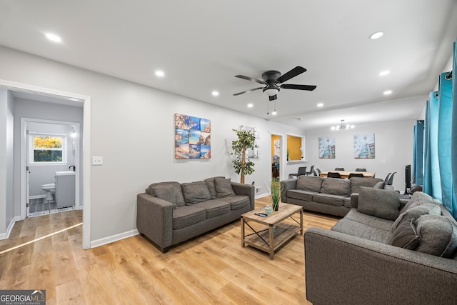 living room with light hardwood / wood-style floors and ceiling fan with notable chandelier