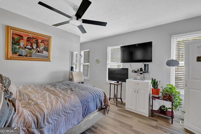 bedroom with multiple windows, a textured ceiling, light hardwood / wood-style floors, and ceiling fan