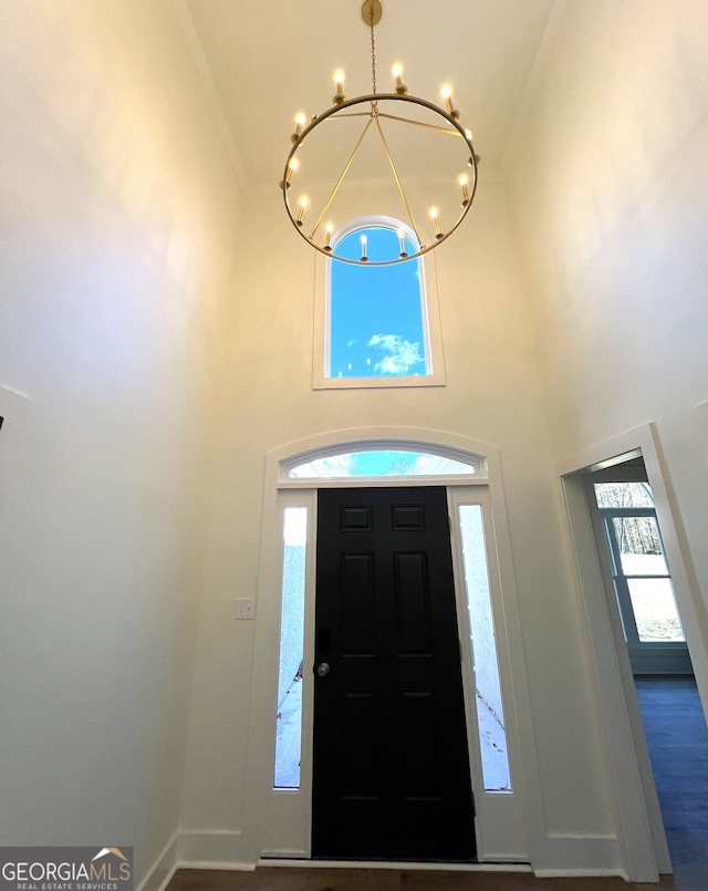 entryway with wood-type flooring, a notable chandelier, ornamental molding, and a high ceiling