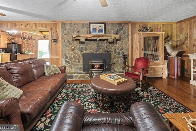 living room with wood walls, a wood stove, ceiling fan, a textured ceiling, and wood-type flooring