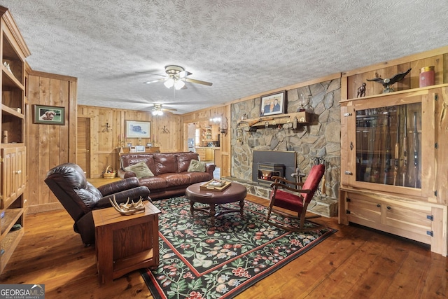 living room with a textured ceiling, a stone fireplace, wooden walls, and dark hardwood / wood-style floors