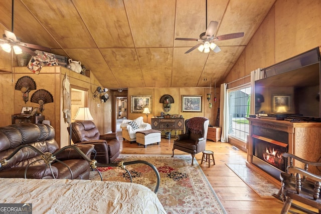 living room with light wood-type flooring, ceiling fan, lofted ceiling, and wood walls