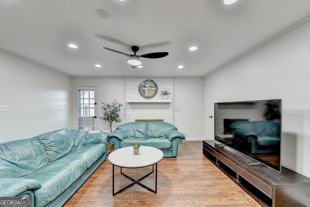 living room with a brick fireplace, ceiling fan, ornamental molding, and light hardwood / wood-style flooring