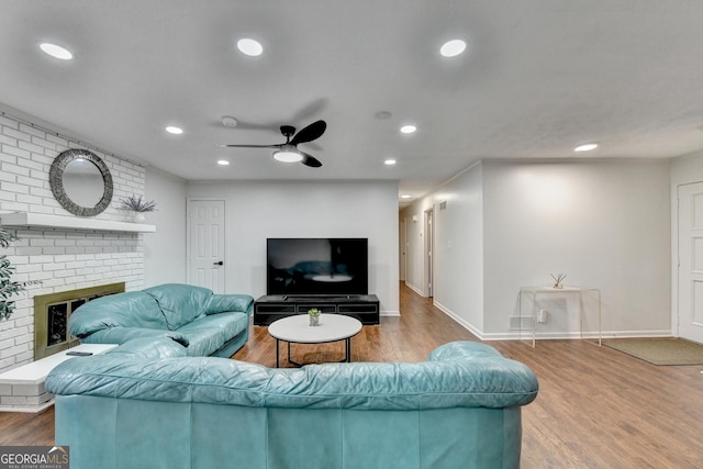 living room with ceiling fan, wood-type flooring, and a brick fireplace