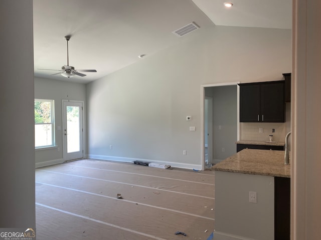 kitchen featuring decorative backsplash, ceiling fan, light stone counters, and vaulted ceiling