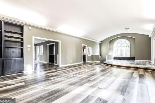 unfurnished living room featuring built in shelves, hardwood / wood-style flooring, and vaulted ceiling