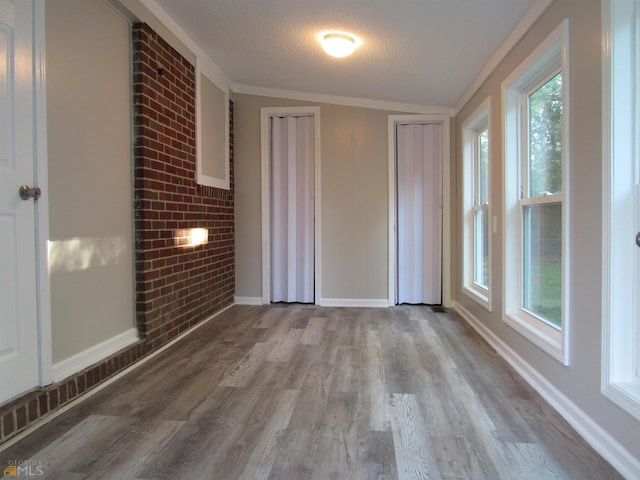 empty room featuring lofted ceiling, crown molding, a textured ceiling, light hardwood / wood-style floors, and brick wall