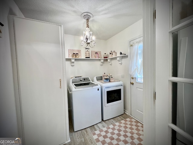 clothes washing area with a chandelier, a textured ceiling, light hardwood / wood-style floors, and washing machine and clothes dryer