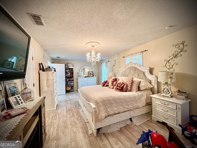 bedroom with an inviting chandelier, a textured ceiling, and light hardwood / wood-style flooring