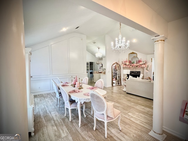 dining area featuring light wood-type flooring, vaulted ceiling, a notable chandelier, and ornate columns