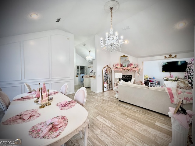 dining space with a notable chandelier, light hardwood / wood-style floors, and vaulted ceiling