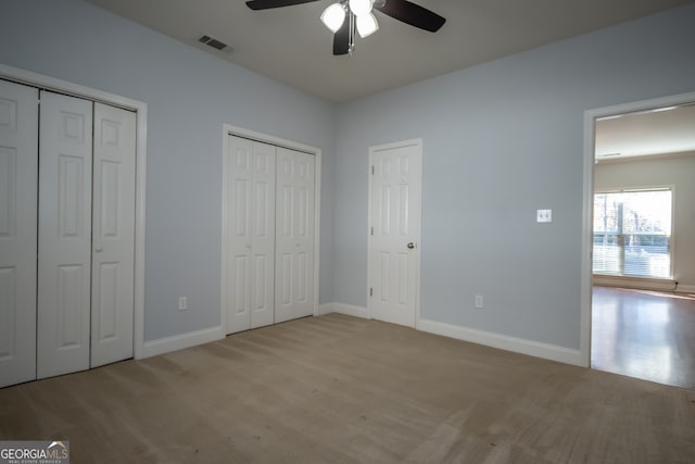 unfurnished bedroom featuring ceiling fan, light colored carpet, and multiple closets