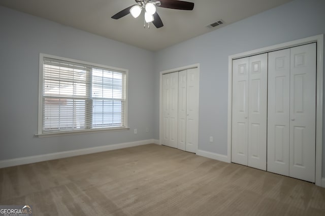 unfurnished bedroom with ceiling fan, light hardwood / wood-style floors, and two closets