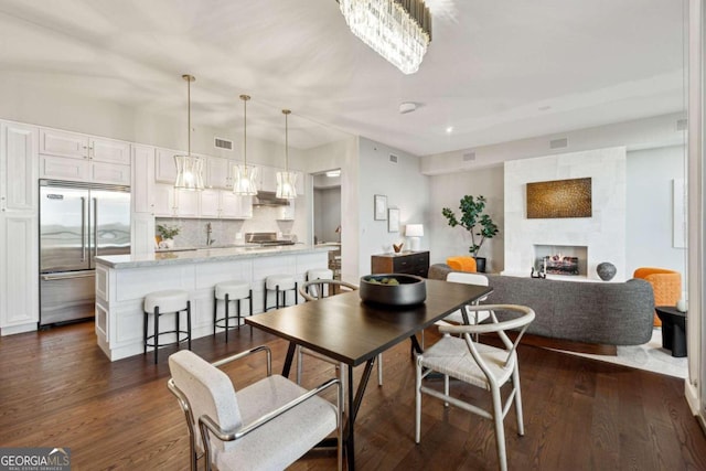 dining area with a large fireplace, dark wood-type flooring, and a notable chandelier