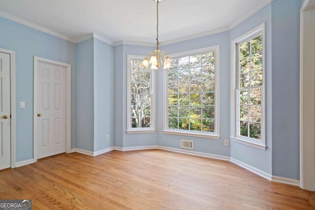 unfurnished dining area featuring light hardwood / wood-style floors, crown molding, and a chandelier