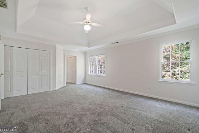 unfurnished bedroom with a closet, carpet floors, a tray ceiling, and ceiling fan