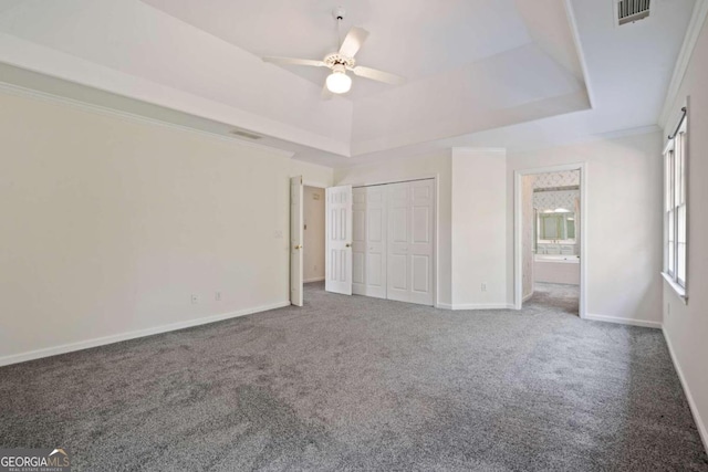 unfurnished bedroom featuring a raised ceiling, crown molding, ensuite bath, ceiling fan, and carpet floors