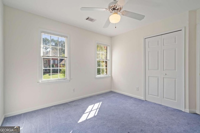 unfurnished bedroom with carpet, a closet, multiple windows, and ceiling fan