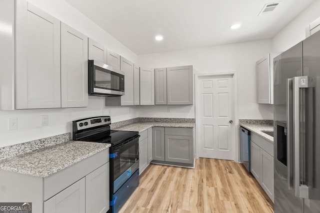 kitchen featuring light stone countertops, appliances with stainless steel finishes, gray cabinets, and light hardwood / wood-style floors