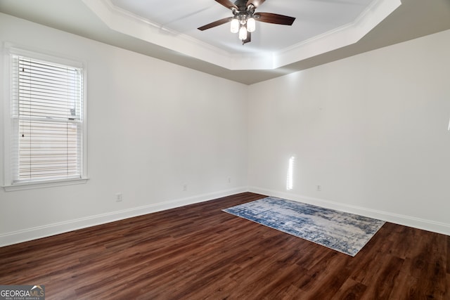 spare room with a raised ceiling, ceiling fan, dark wood-type flooring, and crown molding