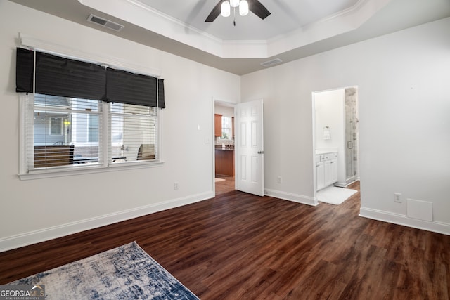 unfurnished bedroom featuring ceiling fan, dark wood-type flooring, crown molding, ensuite bathroom, and a tray ceiling