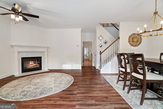 dining room with ceiling fan with notable chandelier, dark hardwood / wood-style flooring, crown molding, and a tiled fireplace