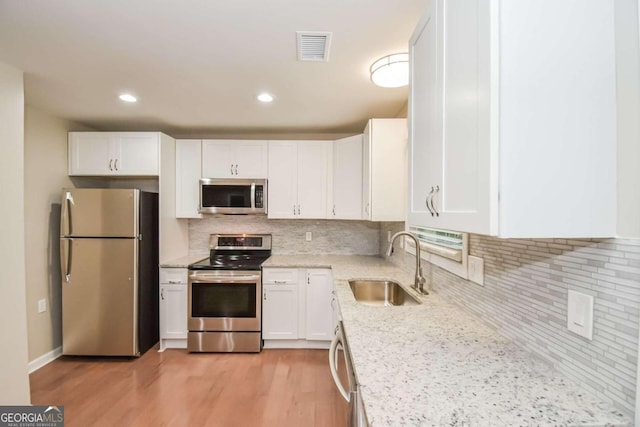 kitchen featuring decorative backsplash, stainless steel appliances, sink, light hardwood / wood-style flooring, and white cabinetry