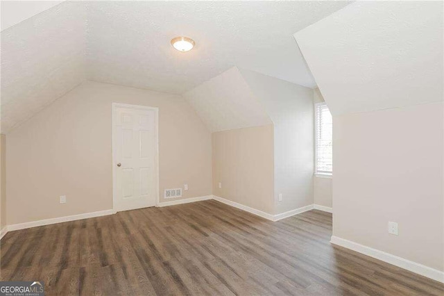 additional living space featuring a textured ceiling, lofted ceiling, and dark wood-type flooring