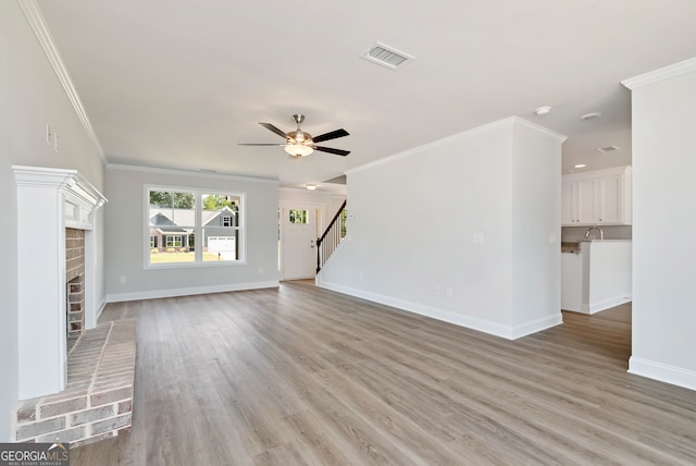 unfurnished living room featuring a fireplace, light wood-type flooring, ceiling fan, and ornamental molding