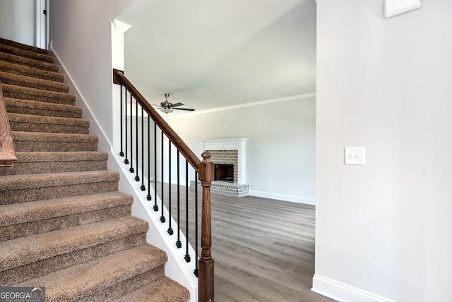 staircase with a fireplace, hardwood / wood-style floors, ceiling fan, and ornamental molding