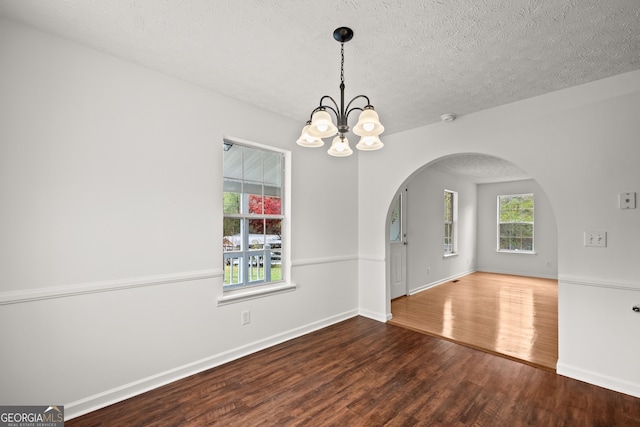 spare room with wood-type flooring, a textured ceiling, a wealth of natural light, and a notable chandelier