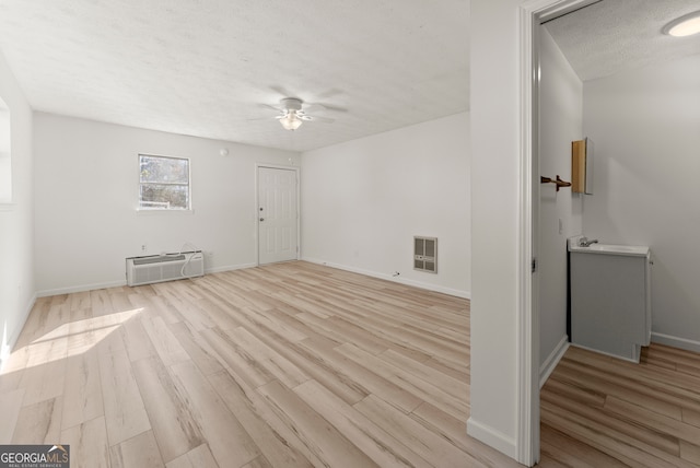 spare room with a wall mounted air conditioner, a textured ceiling, heating unit, ceiling fan, and light hardwood / wood-style floors