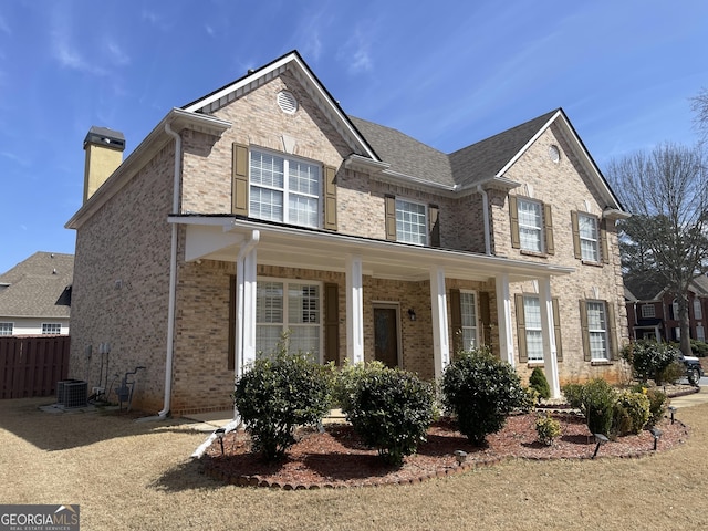 view of front of home with brick siding, a chimney, a porch, and fence