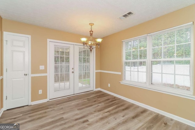 unfurnished dining area with a chandelier, hardwood / wood-style floors, a textured ceiling, and french doors