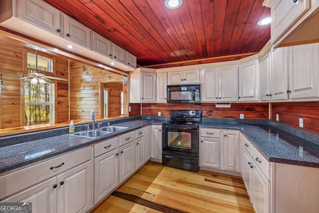 kitchen with wooden walls, sink, black appliances, light hardwood / wood-style floors, and white cabinetry