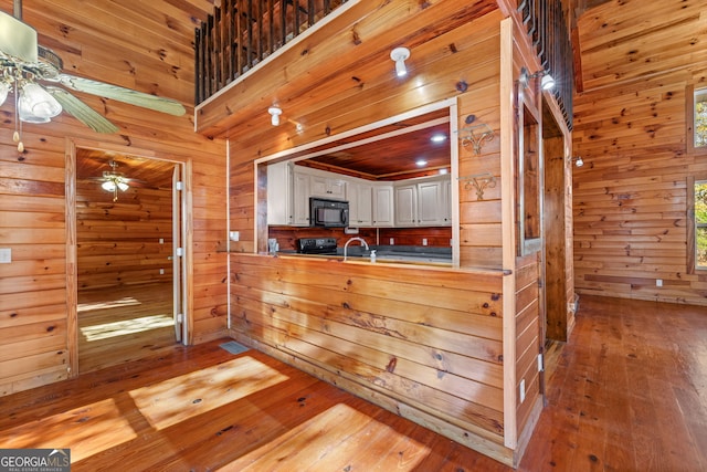 kitchen featuring white cabinetry, kitchen peninsula, wood walls, light hardwood / wood-style floors, and black appliances