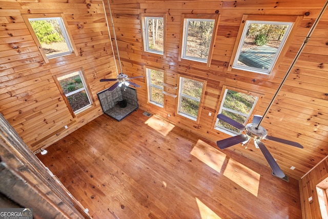 unfurnished living room with wooden walls, hardwood / wood-style floors, ceiling fan, and a healthy amount of sunlight