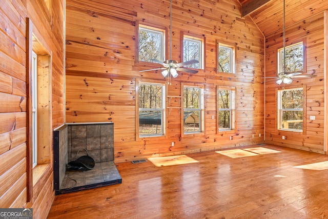 unfurnished living room featuring ceiling fan, wooden walls, beam ceiling, wood-type flooring, and high vaulted ceiling