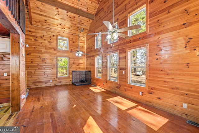 unfurnished living room featuring wooden walls, high vaulted ceiling, and light hardwood / wood-style flooring