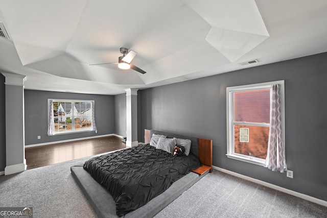 carpeted bedroom with ceiling fan, a tray ceiling, and decorative columns